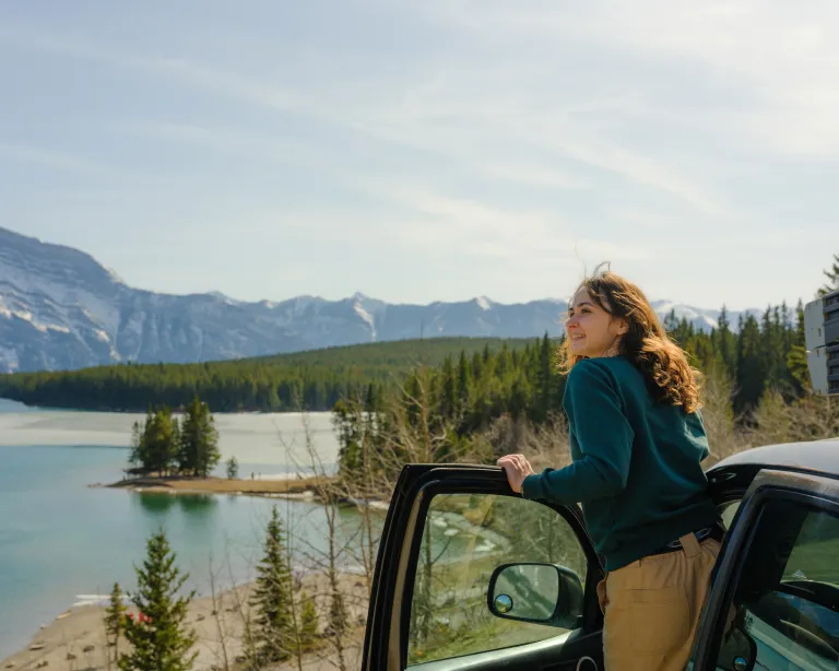 Young woman enjoying a scenic mountain lake view beside a car.