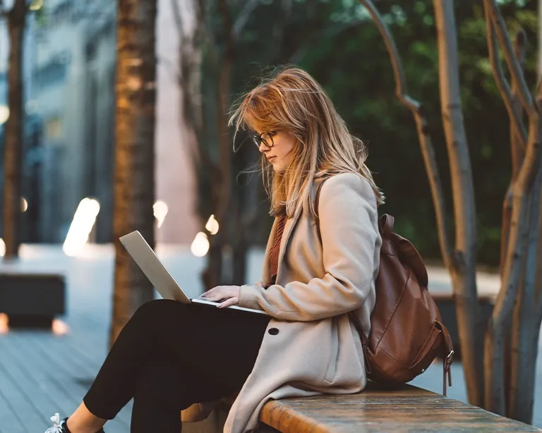 Young woman sitting outdoors and studying for IELTS exam using a laptop.