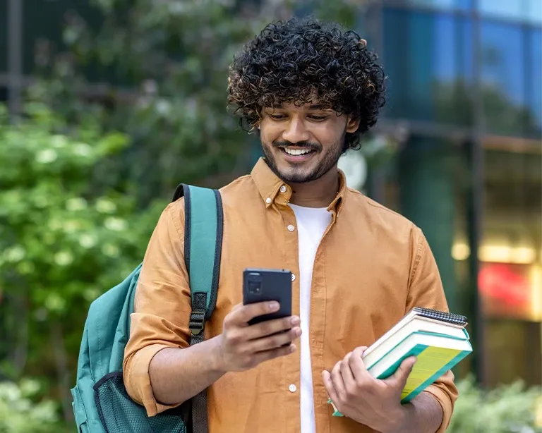 Young man holding study materials and checking his phone while preparing for the IELTS exam.