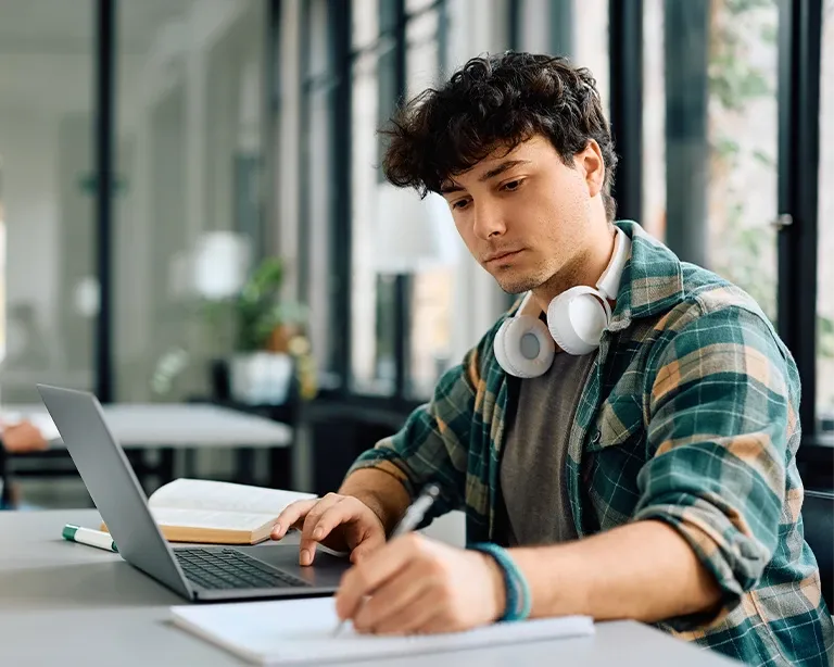 A boy taking notes while studying and preparing for IELTS exam online