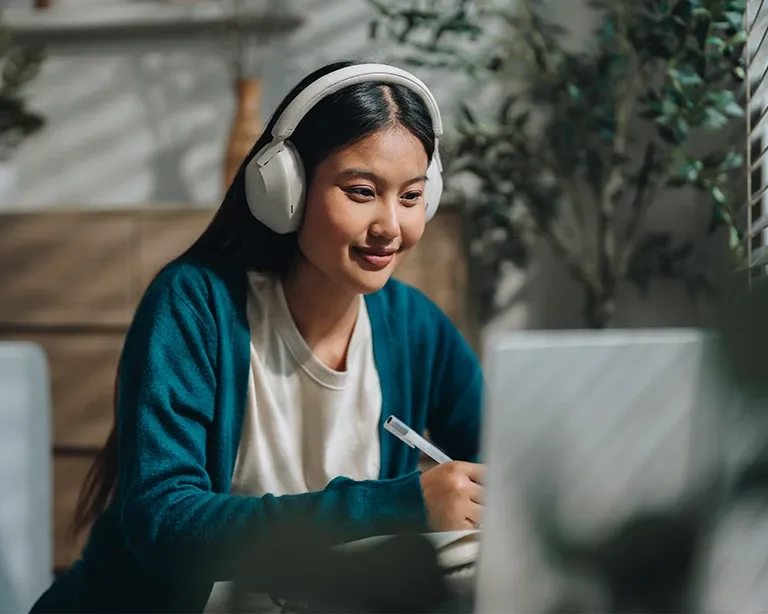 A girl using headphones and laptop to study for her IELTS examination using preparation resources