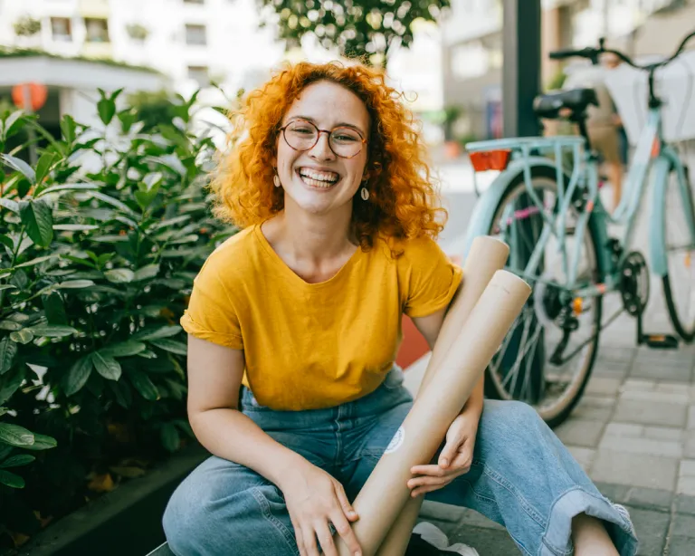 Smiling student sitting outdoors holding study materials near a bicycle.