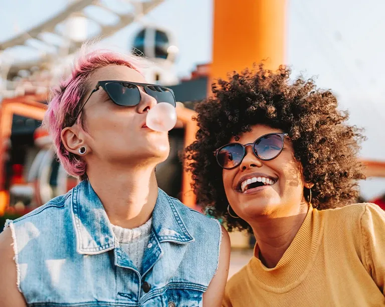 Two friends wearing sunglasses smiling together outdoors on a sunny day