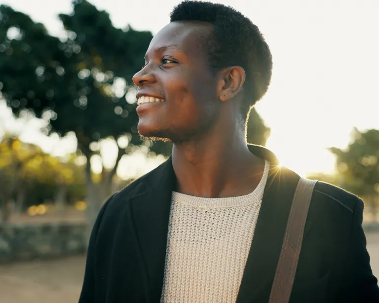 Young man smiling with a shoulder bag during sunset