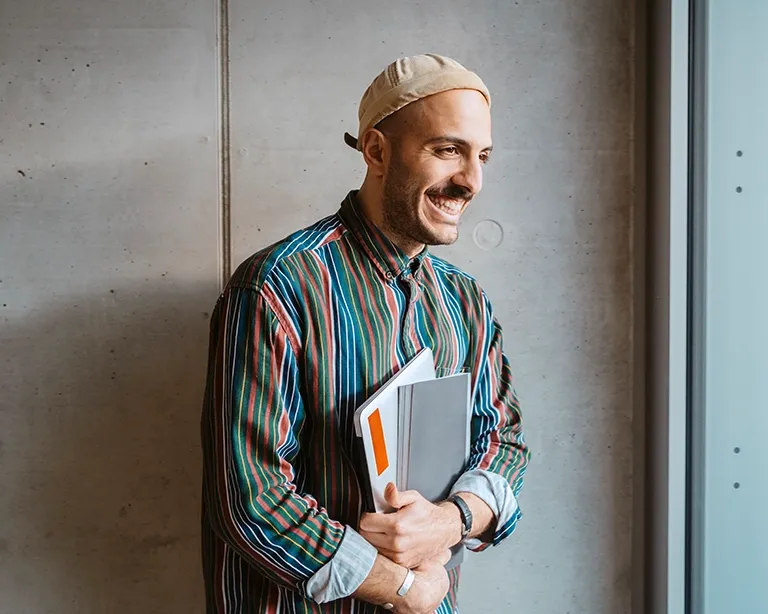 Smiling man holding study materials while standing indoors.