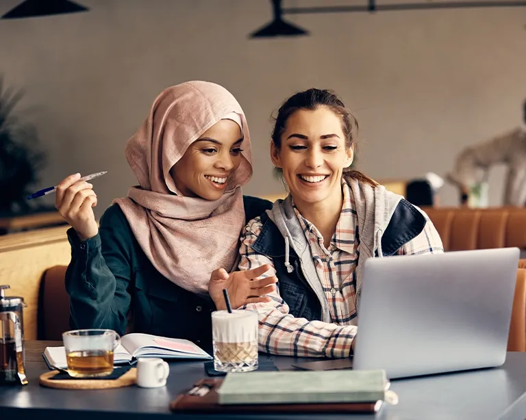 Two students studying together online for the IELTS exam using a laptop.