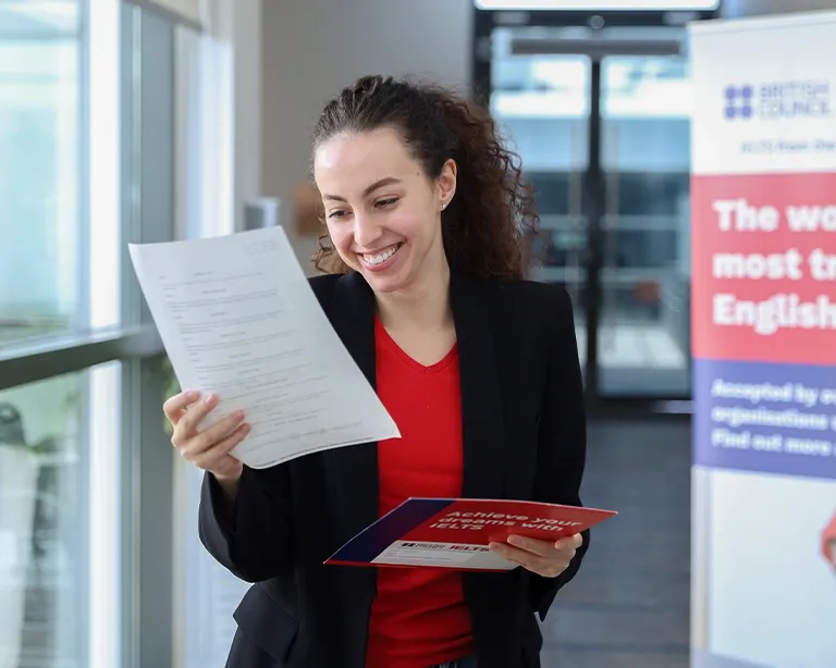 Woman smiling while checking IELTS study materials at an IELTS center.