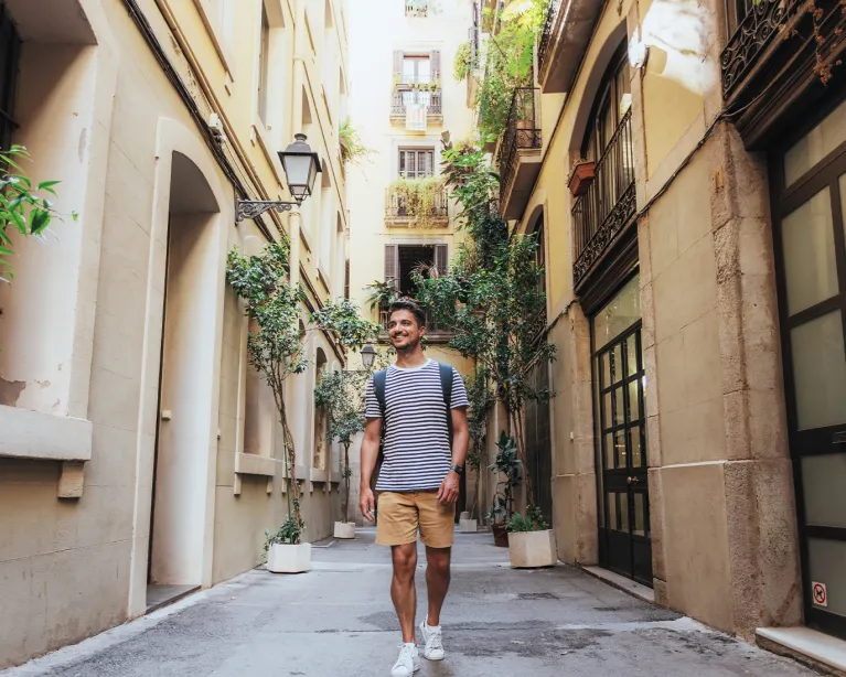 Young man with a backpack walking through a narrow European street.