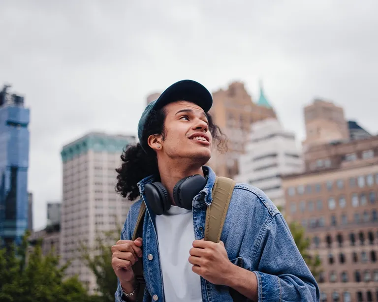 Young man with headphones and a backpack smiling on a city street.