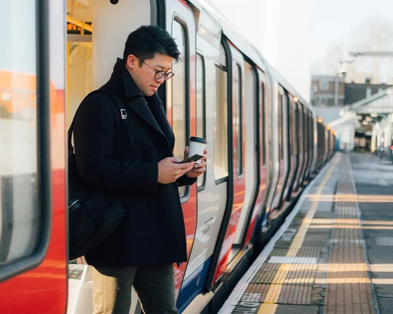 Young man using a mobile phone while standing beside a train at a station.