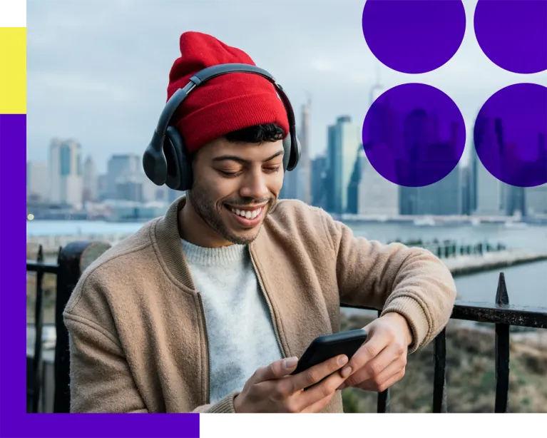 Young man wearing a winter hat while using her mobile phone near a city waterfront.
