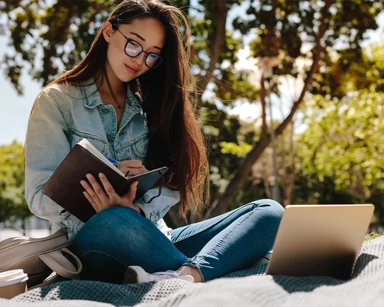 Young woman reading a book for IELTS exam while sitting outdoors in a park.
