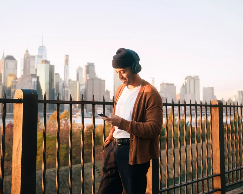 Person standing near a city viewpoint while using a mobile phone