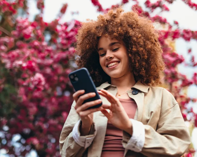 young-woman-curly-hair-smartphone-blooming-trees